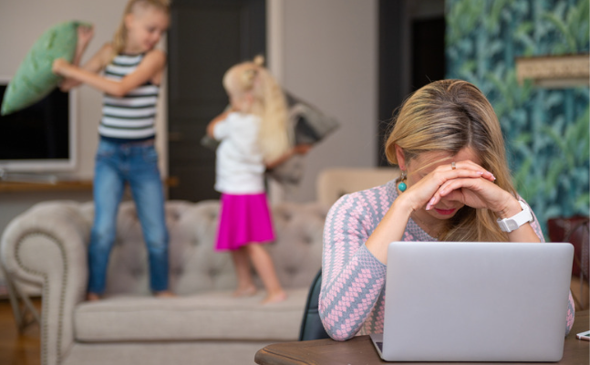 Eine Frau verkörpert Geduld im Familienalltag, während sie mit ihren Kindern im Hintergrund vor einem Laptop sitzt.