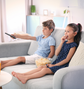 Zwei Kinder, die auf einer Couch sitzen und sich eine Fernsehwerbung ansehen, sind Manipulationen ausgesetzt.