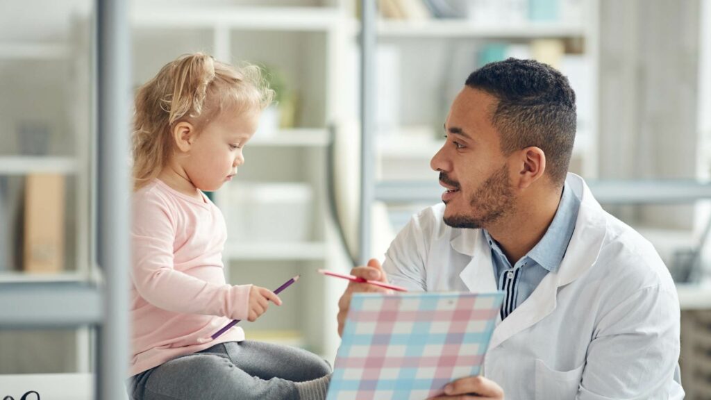 Ein Kinderarzt spricht mit einem kleinen Mädchen in einer Arztpraxis.