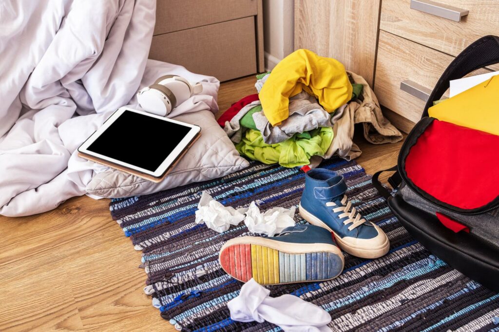 Das unordentliche Zimmer eines Teenagers mit einem Koffer, Kleidung und einem Tablet verstreut.