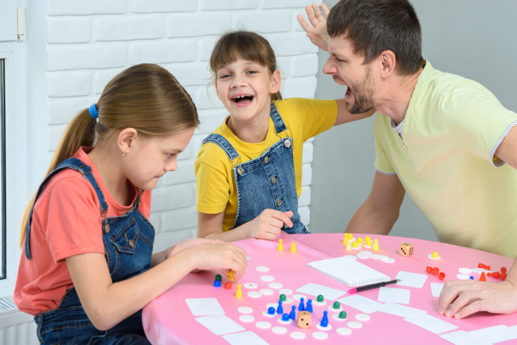 Ein Mann und seine Kinder spielen ein Würfelspiel und demonstrieren damit emotionale Intelligenz im Familienleben.